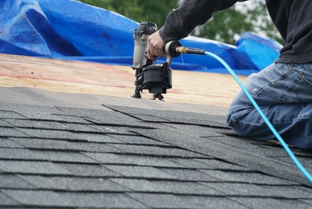 worker installing shingle tiles on roof